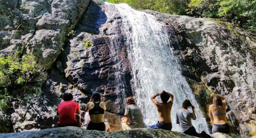 A group of students sit on a rock near a large waterfall